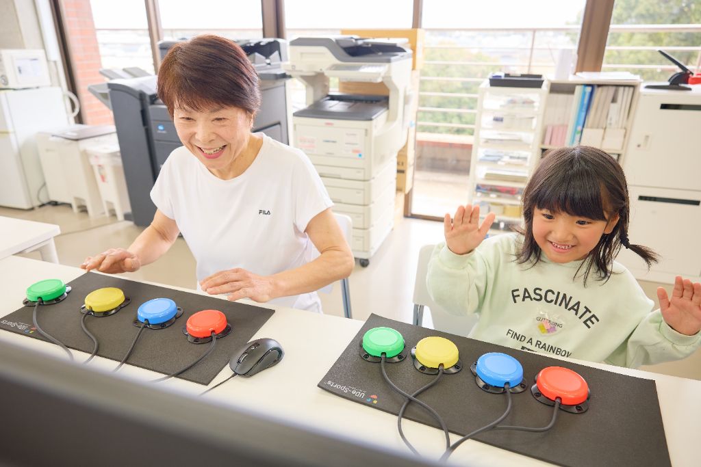 高齢者とお子様がUDe-スポーツのカラーボタンで楽しくゲームをしている様子